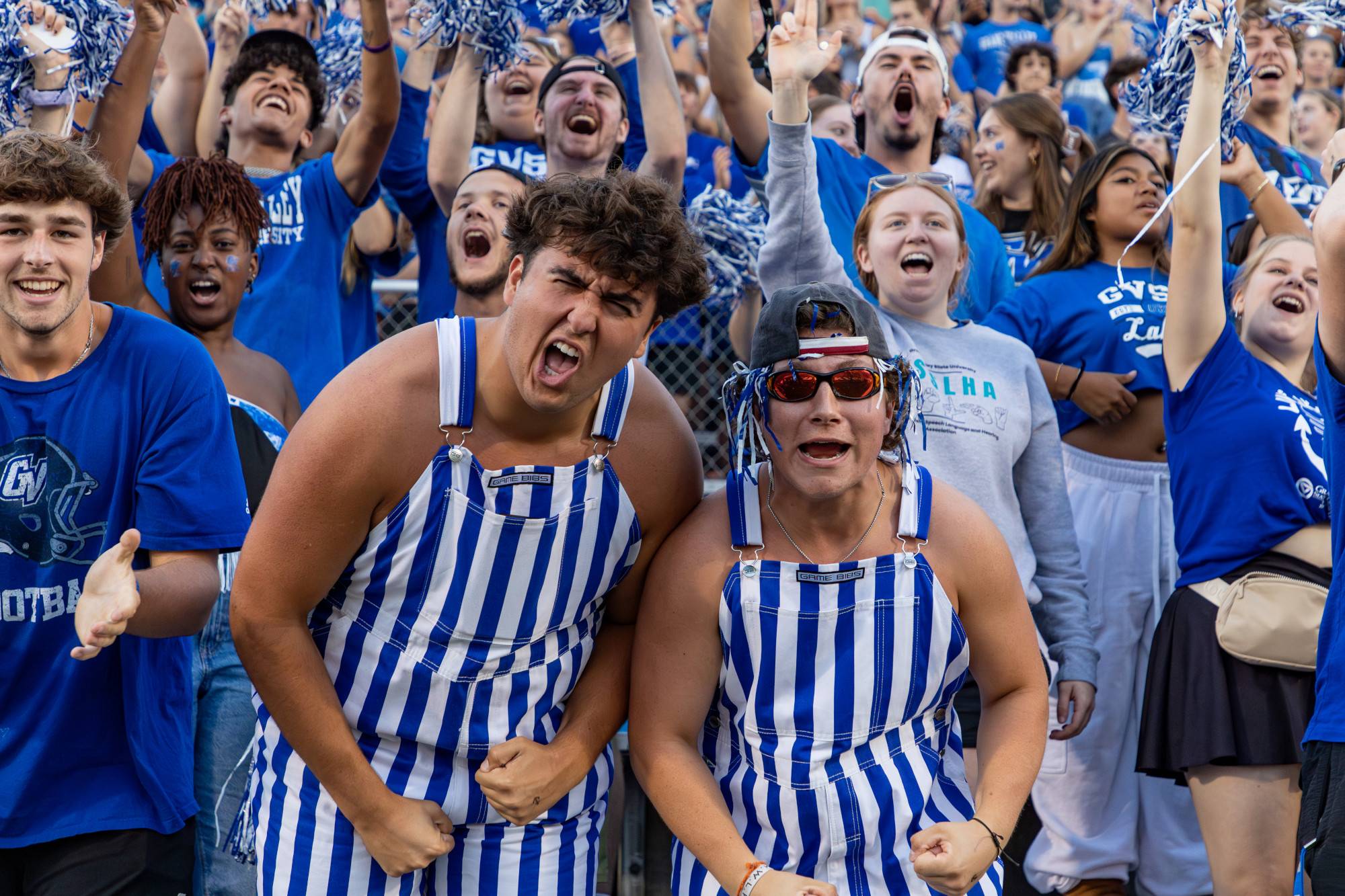 Two Lakers cheer on the GVSU Football team wearing blue and white striped overalls